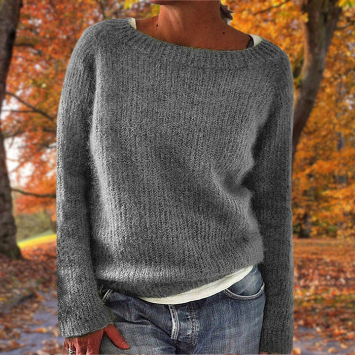 Szürke színű, finom szövésű, hosszú ujjú kötött pulóver farmerrel, modellen elölnézetből, őszi fák között. 4