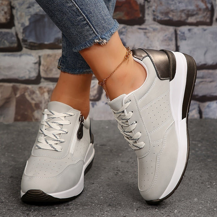 Világosszürke, lyukacsos felsőrészű sneaker fehér-fekete fűzővel, két lábon, elölről és oldalról látszik 5
