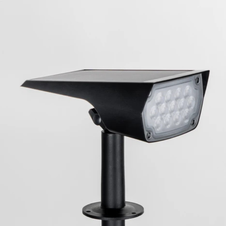 Fekete spotlámpa közelről fehér háttér előtt: elöl a LED-es lencse, felül a napelemes panel, alatta a rövid szár. 4