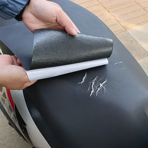 A fekete folt védőpapírját lehúzzák, mielőtt a motorülés karcos, repedt felületére ragasztják 3
