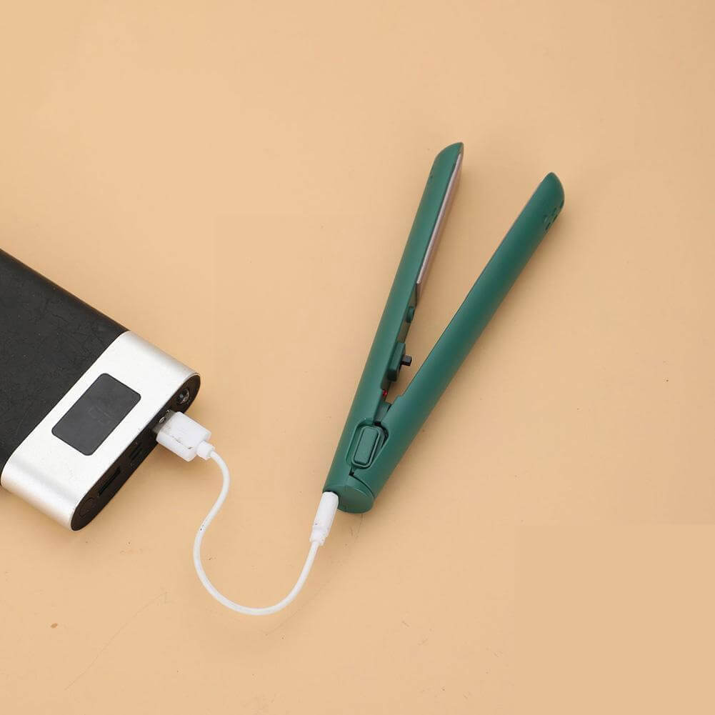 A zöld, kinyitott hajvasaló USB-kábellel egy külső akkumulátorhoz csatlakoztatva, barackszínű háttéren. 1