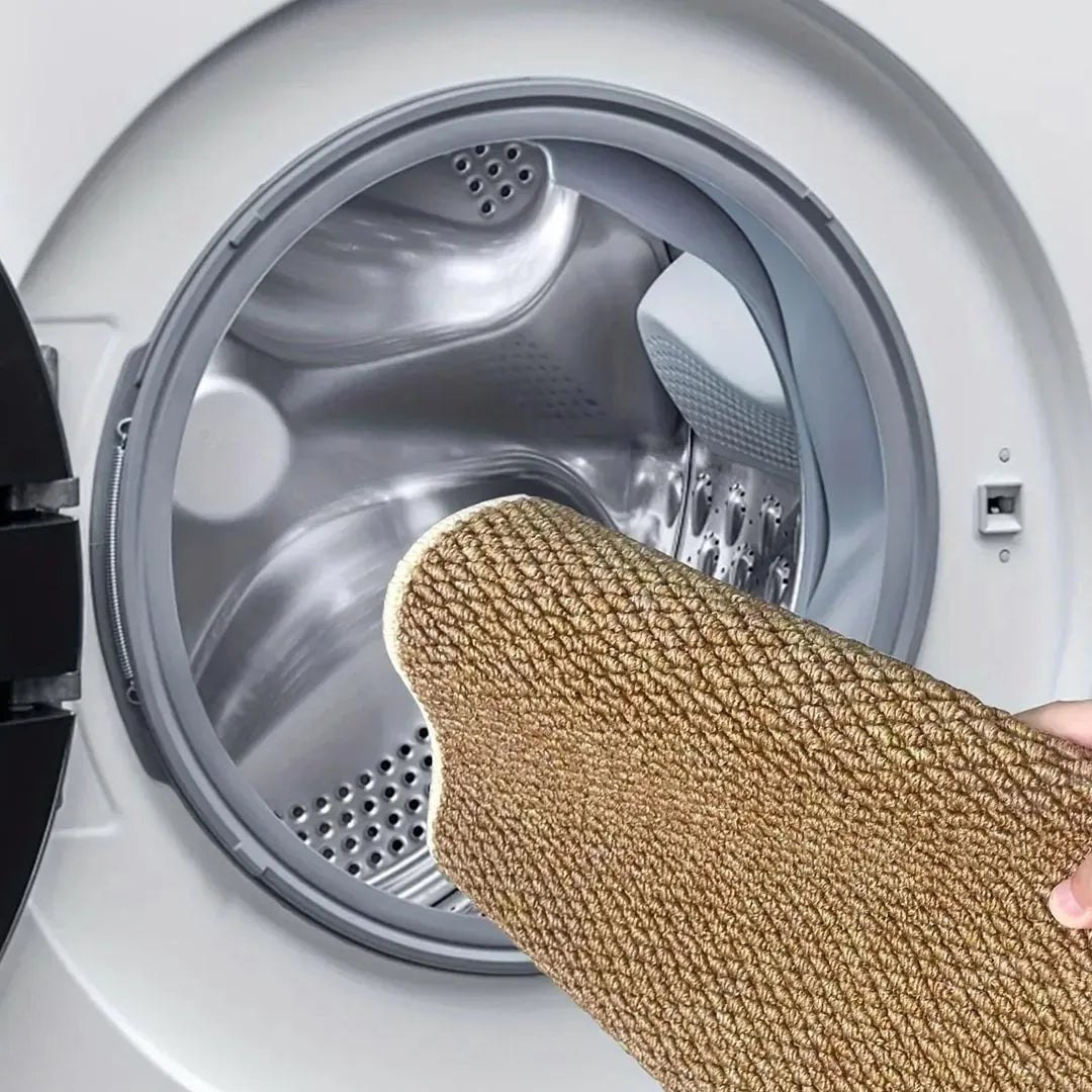 Barna szőnyeget egy kéz hajtogatva tol a nyitott mosógép dobjába, mosásra készülve 7