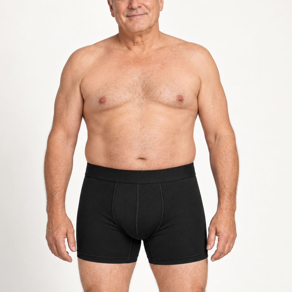 Idősebb, mosolygó férfi modell szemből fekete boxeralsóban, természetes testalkattal, fehér háttér előtt. 2