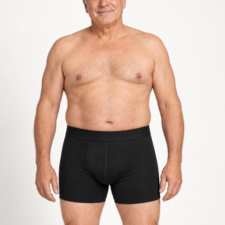 Idősebb, mosolygó férfi modell szemből fekete boxeralsóban, természetes testalkattal, fehér háttér előtt. 2