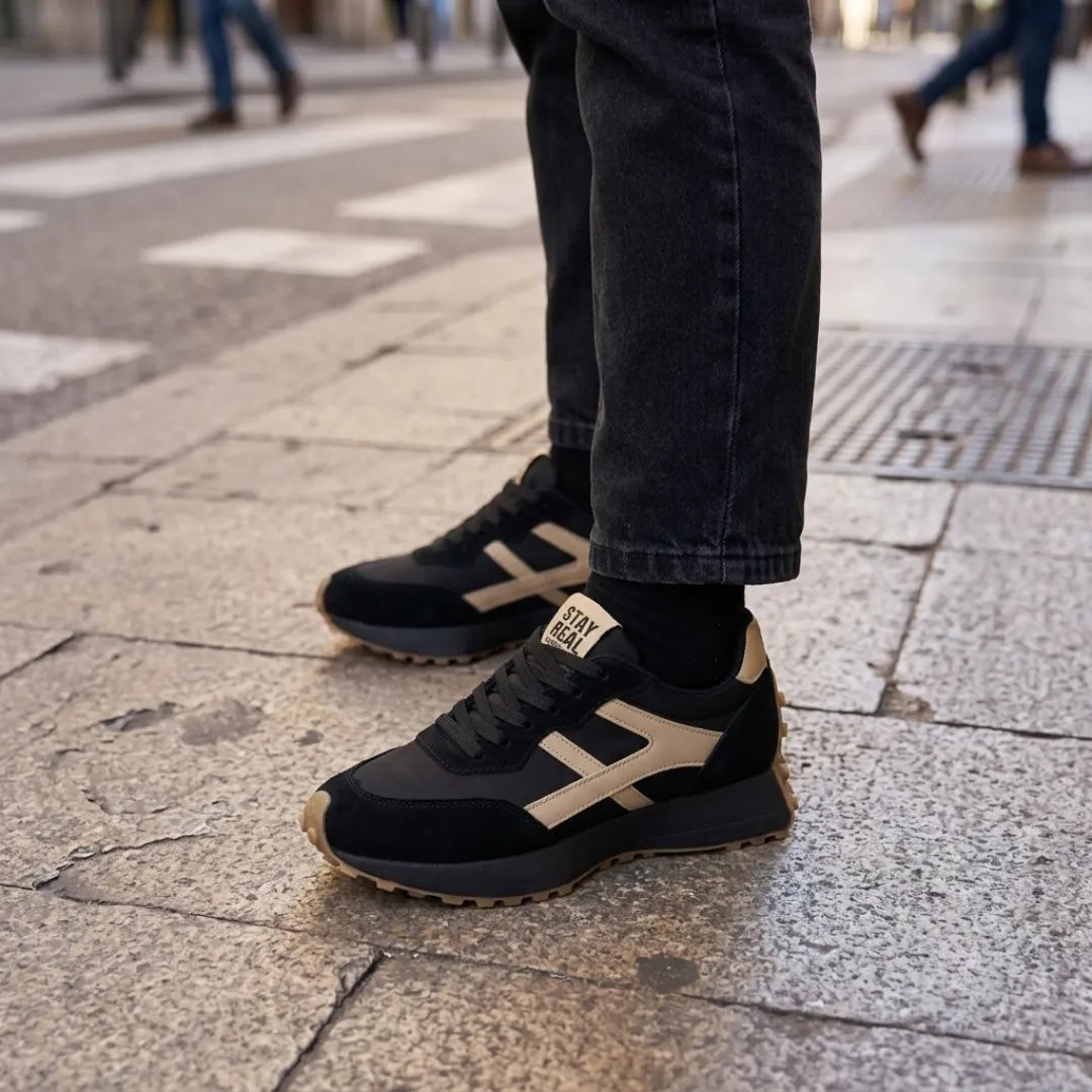 Fekete sneaker krémszínű díszítéssel lábon, farmerrel egy járdán állva 17