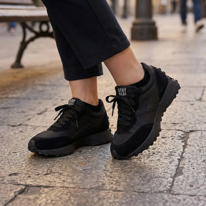 Fekete sneaker lábon, sötét nadrággal sétálva macskaköves utcán 7