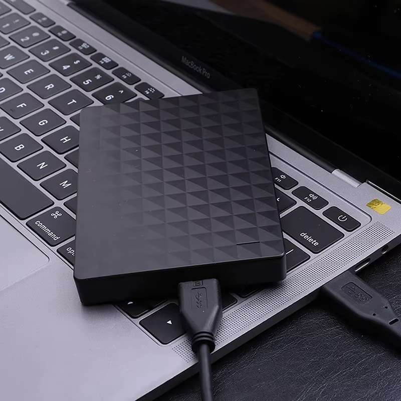 A fekete külső merevlemez egy laptop billentyűzetén fekszik, USB-kábellel csatlakoztatva a géphez 3