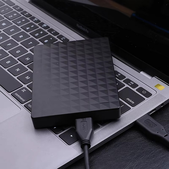 A fekete külső merevlemez egy laptop billentyűzetén fekszik, USB-kábellel csatlakoztatva a géphez 3