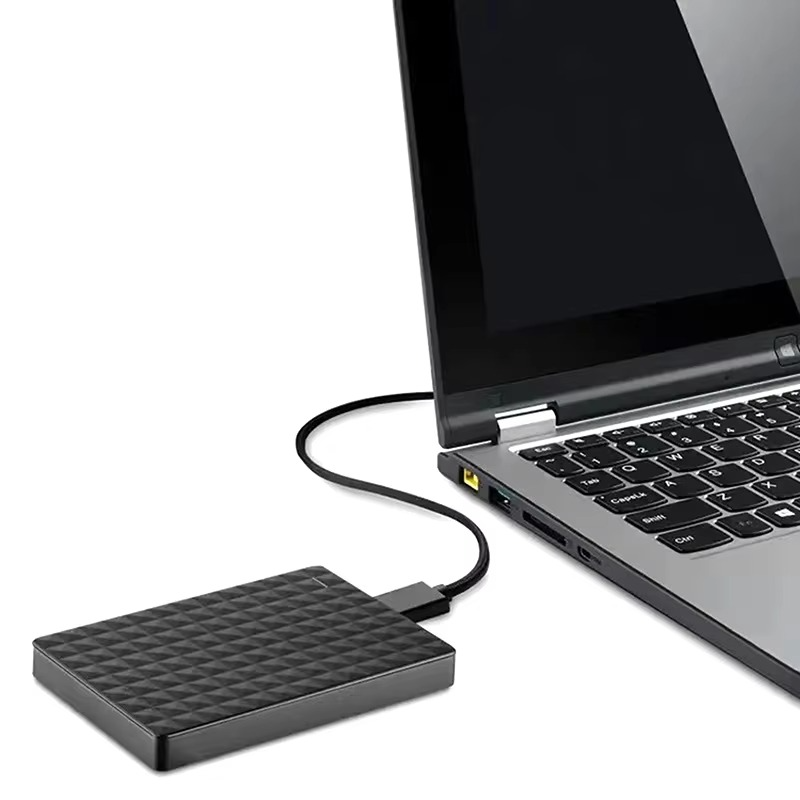 A külső merevlemez fehér háttér előtt, kábellel egy nyitott laptop oldalsó USB-portjához csatlakoztatva 5