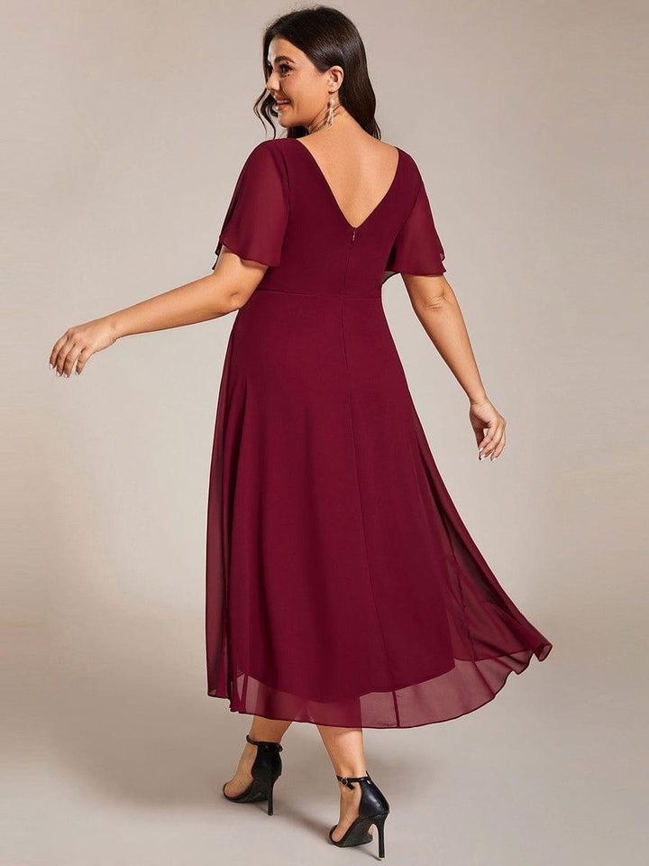 Bordó ruha hátulnézetből plus size modellen: mély V-hátkivágás, cipzár, áttetsző ujjak és hosszabb hátsó szegély. 50