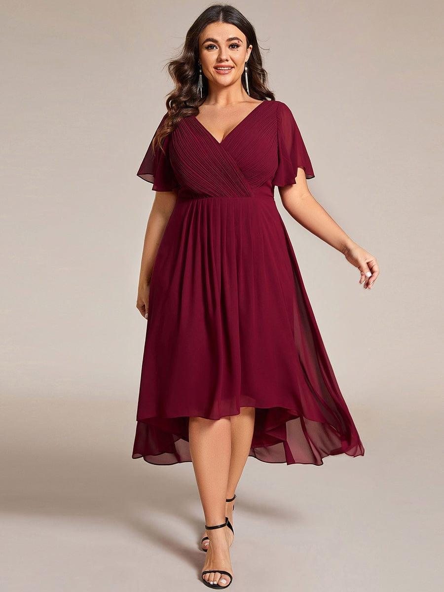 Plus size modell bordó ruhában elölnézetből, fekete szandállal, a magas-alacsony szegély és a fodros ujjak jól látszanak. 49