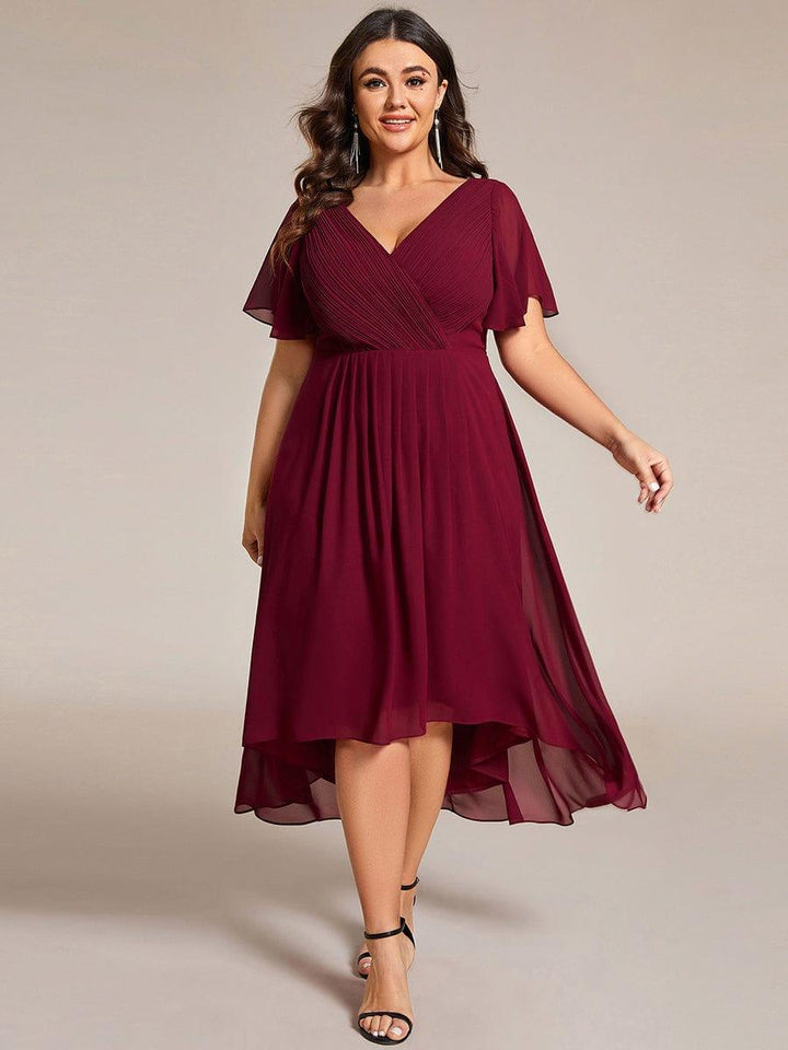 Plus size modell bordó ruhában elölnézetből, fekete szandállal, a magas-alacsony szegély és a fodros ujjak jól látszanak. 49