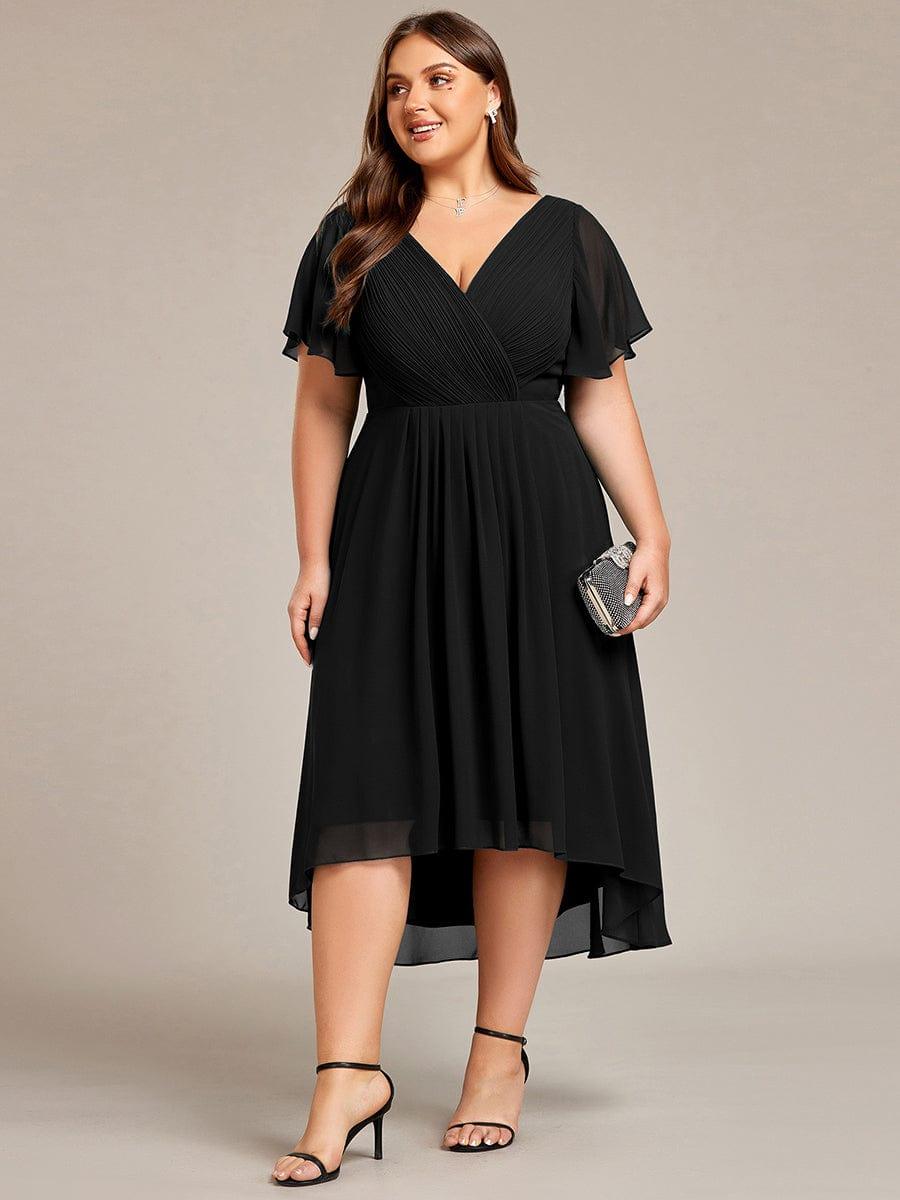 Fekete ruha plus size modellen elölről, kezében csillogó kistáskával, fekete pántos magas sarkú cipőben. 30