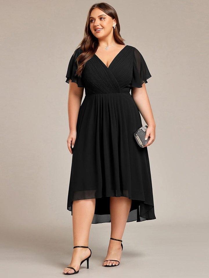 Fekete ruha plus size modellen elölről, kezében csillogó kistáskával, fekete pántos magas sarkú cipőben. 30