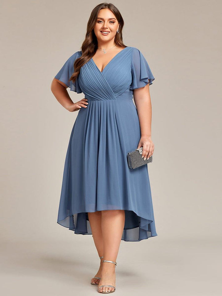 Plus size modell mosolyogva, kezét csípőjére téve, porkék ruhában, a másik kezében csillogó alkalmi kistáskával. 44