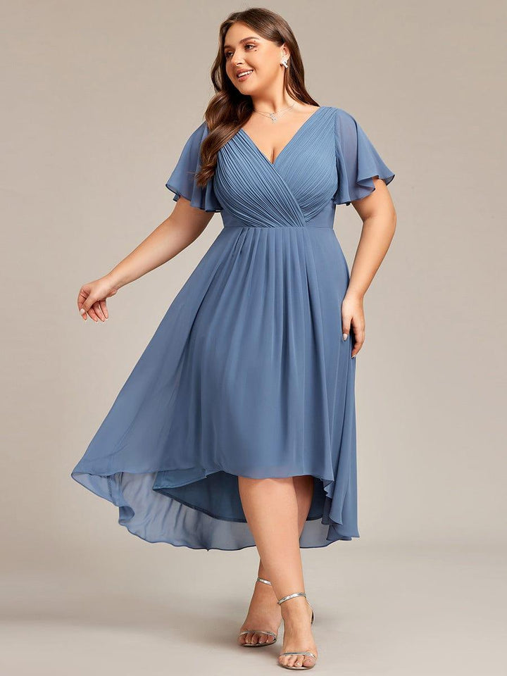 Plus size modell porkék, redőzött V-nyakú, magas-alacsony szabású ruhában, lendületes mozdulattal, ezüst szandálban. 41