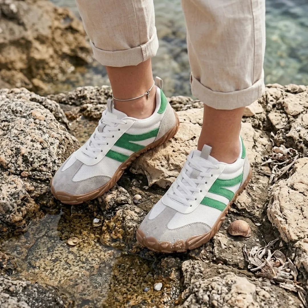 Fehér-zöld barefoot cipőt viselő női láb sziklás tengerparton, felhajtott bézs nadrággal és bokaláncot viselve. 29