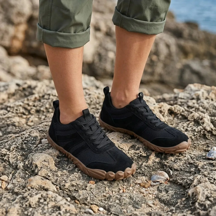 Fekete barefoot cipő viselés közben, zöld felhajtott nadrágos lábakon, tengerparti sziklákon, kagylók mellett. 20