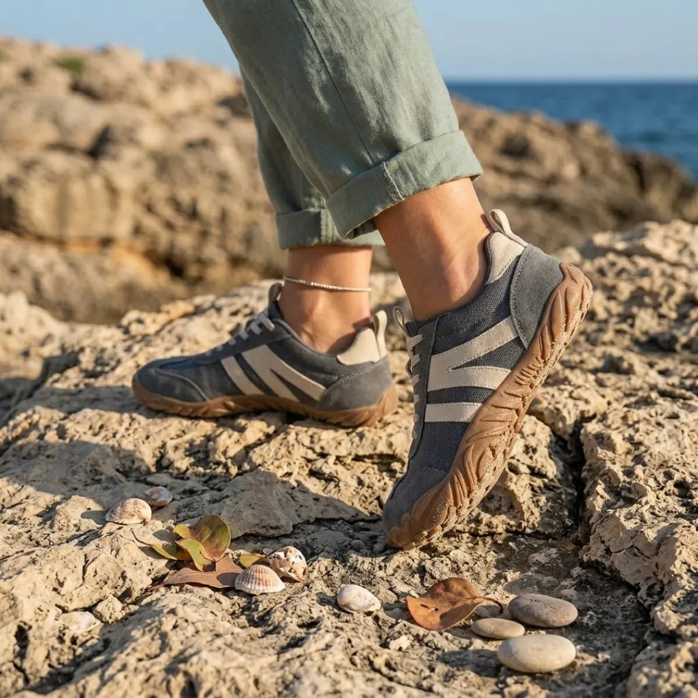 Szürke barefoot cipő viselés közben, felhajtott szárú vászonnadrágos lábakon, tengerparti sziklákon, kagylók és kavicsok között. 2