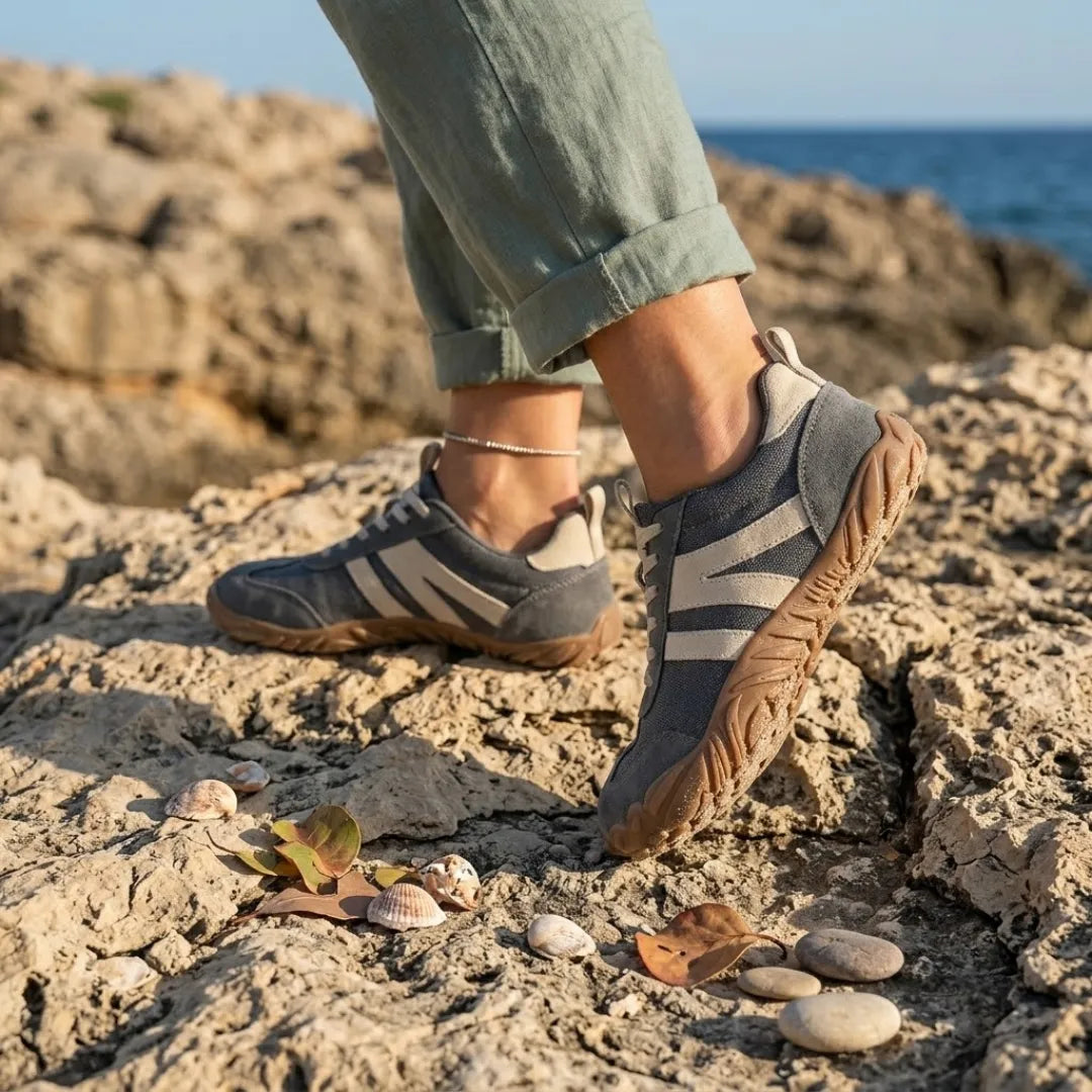 Szürke barefoot cipő viselés közben, felhajtott szárú vászonnadrágos lábakon, tengerparti sziklákon, kagylók és kavicsok között. 2