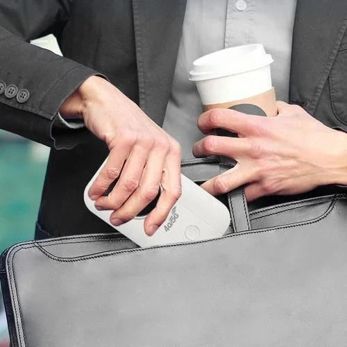 Egy kéz a kicsi fehér routert csúsztatja egy szürke laptoptáskába, a másikban kávéspohár 2