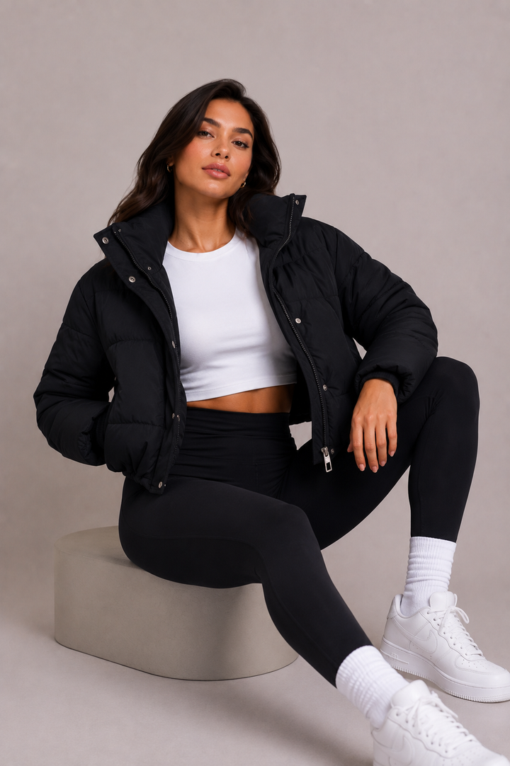 A modell egy szürke dobogón ül, nyitott fekete pufikabátban, fehér crop topban, fekete leggingsben és fehér sportcipőben. 6