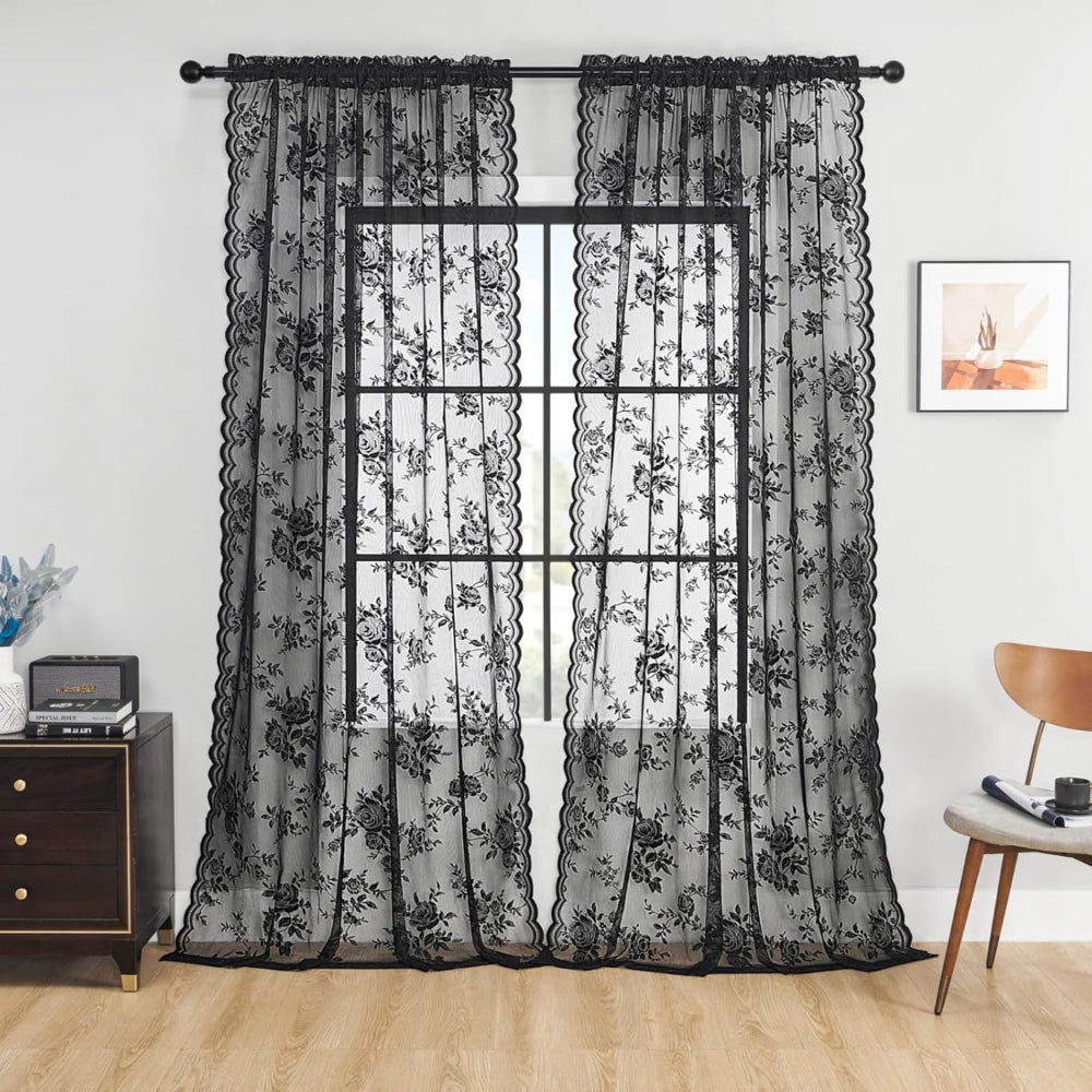 Két fekete, rózsamintás csipkefüggöny rúdkarnison egy világos szobában, komód és fa szék mellett, az ablak előtt lógva. 1