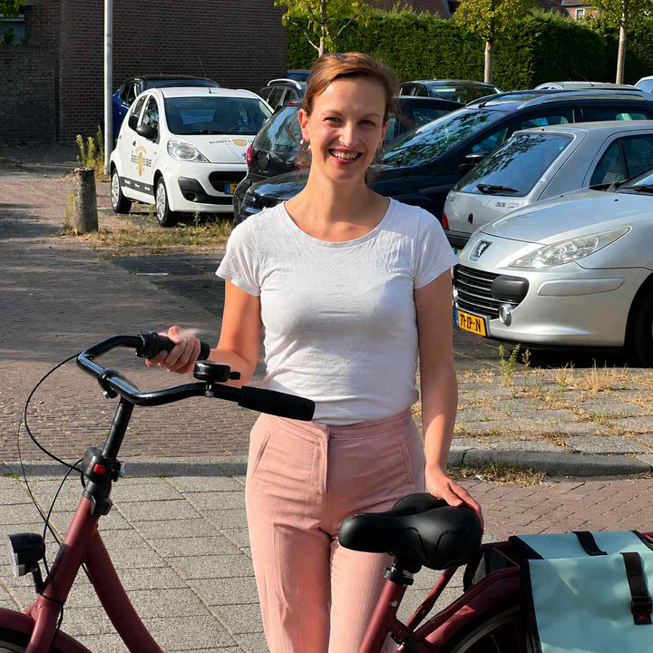 Mosolygó nő áll a piros városi kerékpár mellett, kezét a fekete nyeregen tartja, a kormányon csengő van. 7