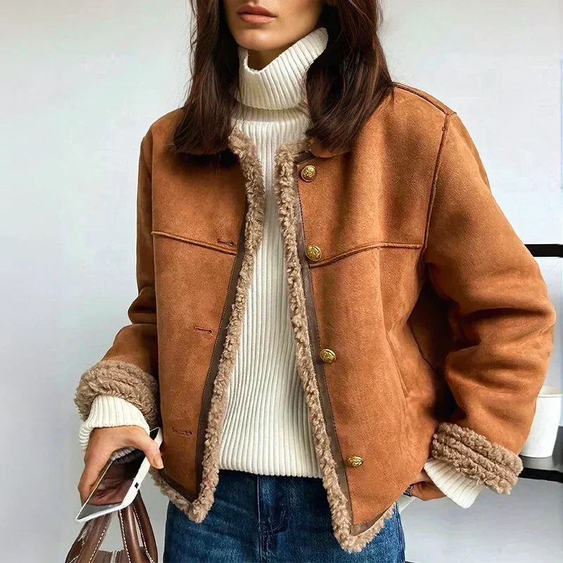 Modell barna shearling kabátban, fehér garbóval és farmerrel, kezében telefon és táska 1