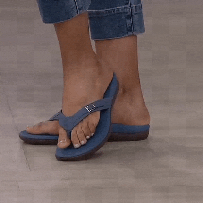 Kék, csatos pántú papucsszandál farmeres modell lábán, szürke padlón, közelről 2