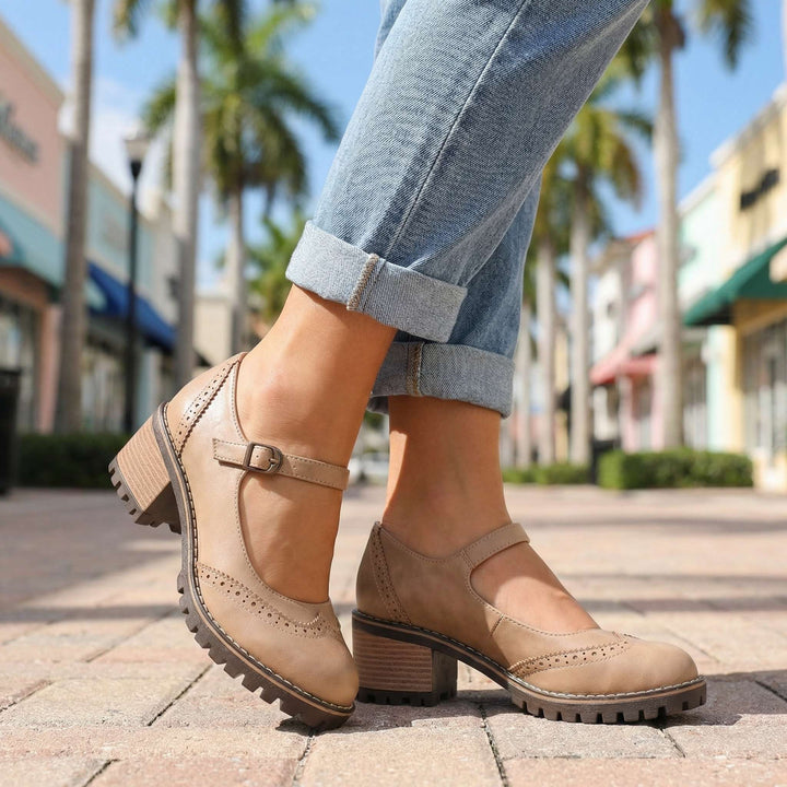 Bézs Mary Jane cipő felhajtott farmerrel viselve, pálmafák és színes üzletek előtt, a csatos pánttal és a lyukacsos díszítéssel. 6