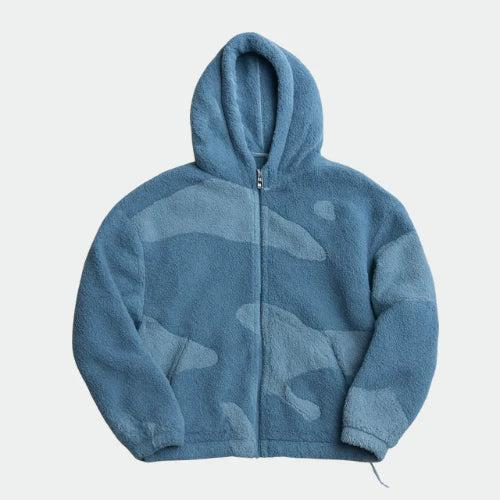 Kék, két árnyalatú bolyhos polárdzseki elölnézetből, cipzárral, kapucnival és finom, camouflage-szerű tónusos mintával. 3
