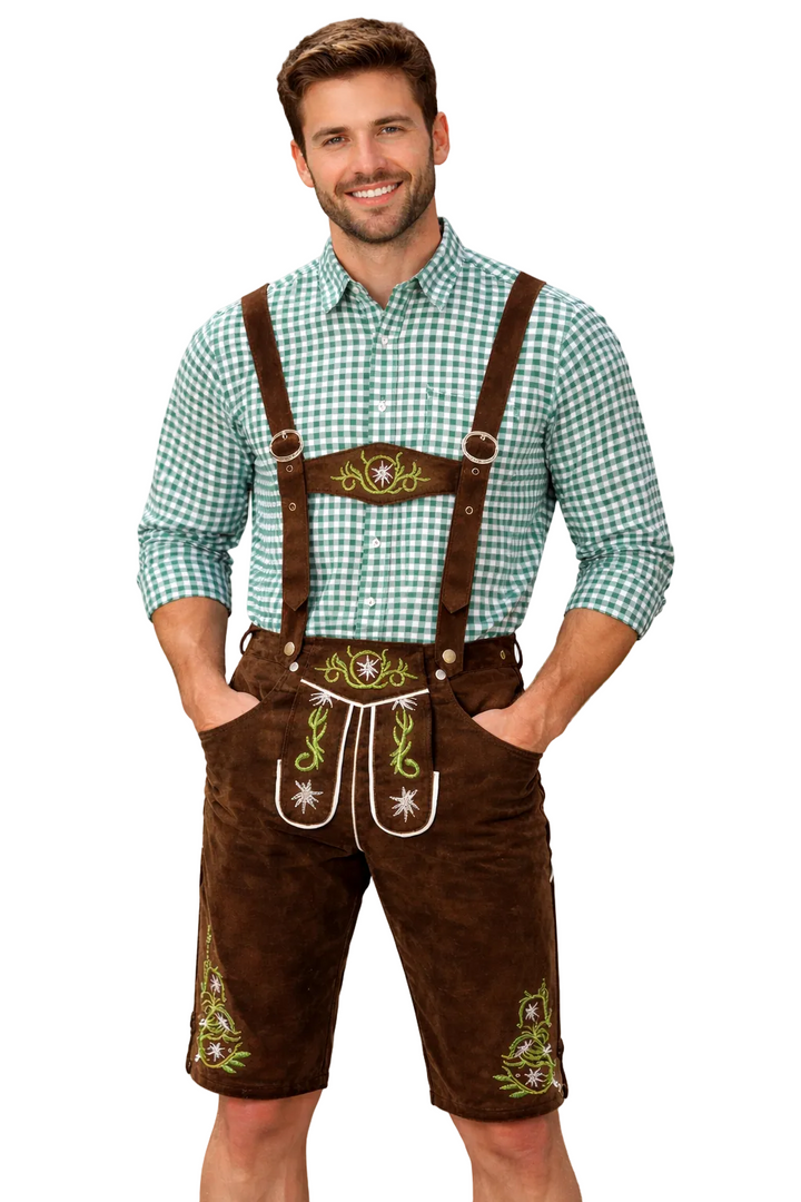 Mosolygó férfi áll szemből, barna, hímzett lederhosent és zöld-fehér kockás inget visel, keze a zsebében, fehér háttér előtt. 1