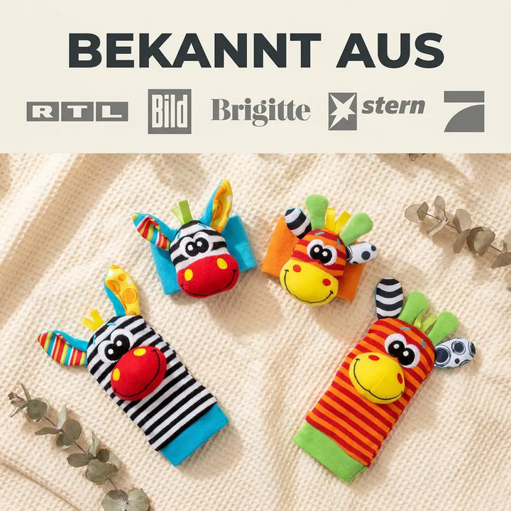 Felülnézet: két csuklópánt és két zokni színes zebra- és zsiráffejjel, krémszínű vaffletextil takarón, eukaliptuszágak között. 7