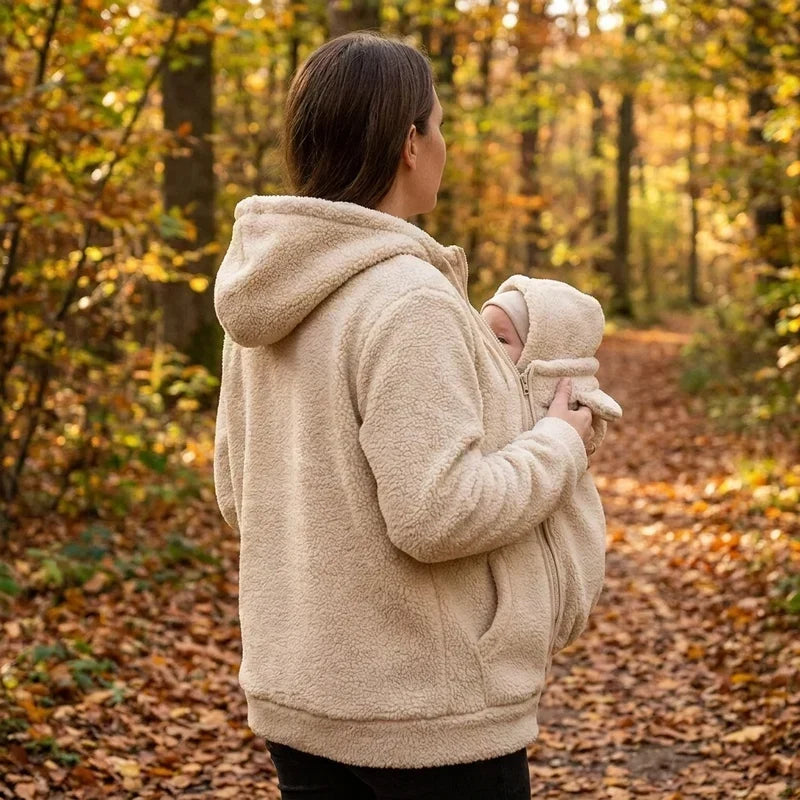 Bézs sherpa felsőt viselő nő hátulról és oldalról, őszi erdőben, a kapucnis hordozóbetétben a babával. 6