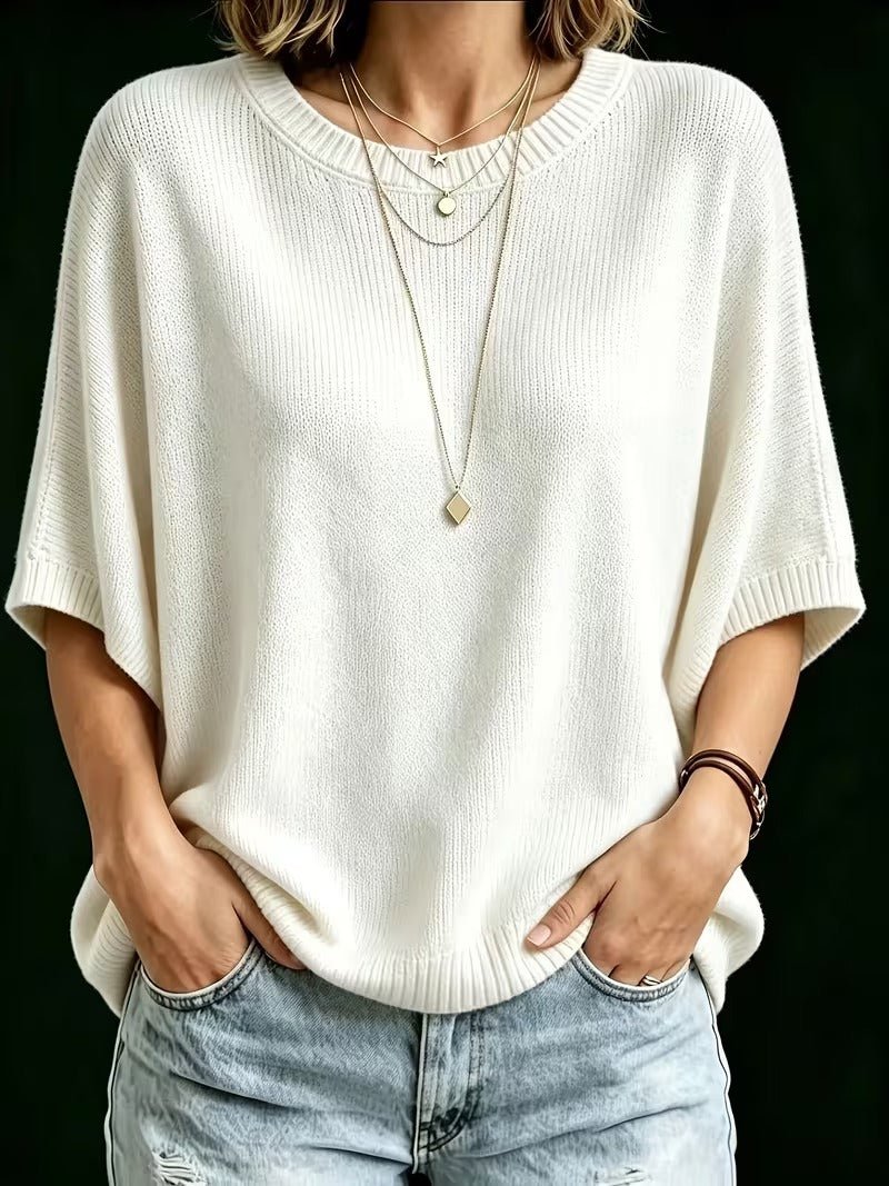Krémfehér denevérujjú kötött felső elölről, mindkét kéz a farmer zsebében, hosszú rombusz medálos nyaklánccal. 23