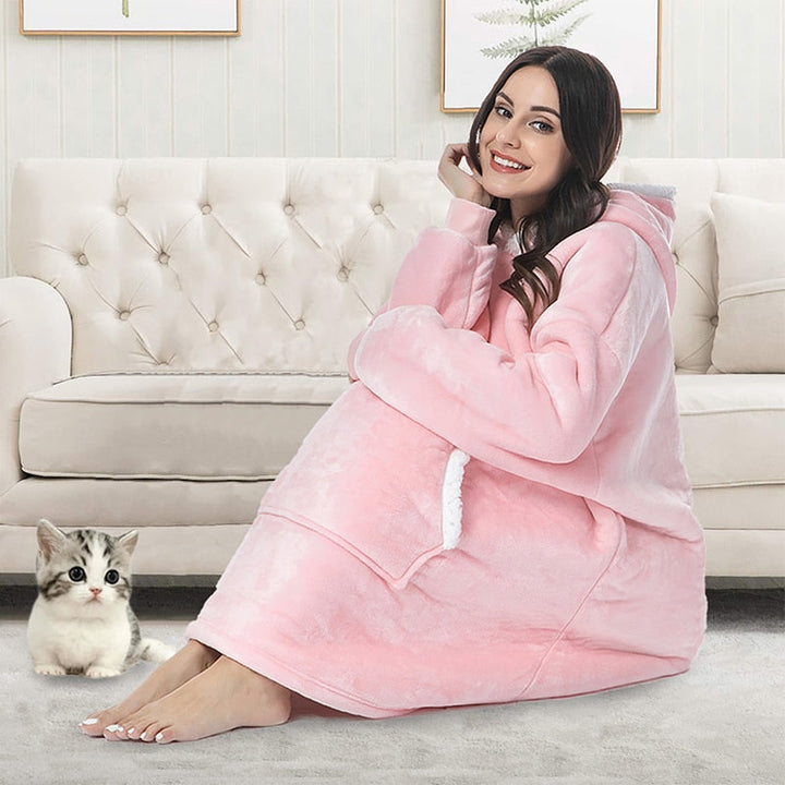 Frau in rosa Kuscheldecke mit Kapuze auf Sofa, gemütlich, Katze, Wohnzimmer, Wintermode.