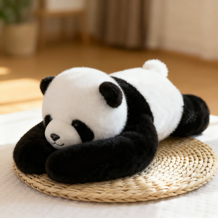 Fekete-fehér panda plüss hasonfekve egy fonott alátéten, hosszú fekete karjaival maga elé ölelve, napfényes szobában. 1