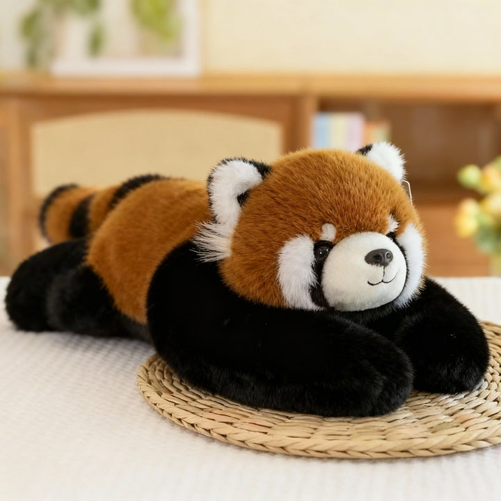 Vörös panda plüss fekve egy fonott alátéten, rókavörös testtel, csíkos farokkal és hosszú fekete karokkal. 13