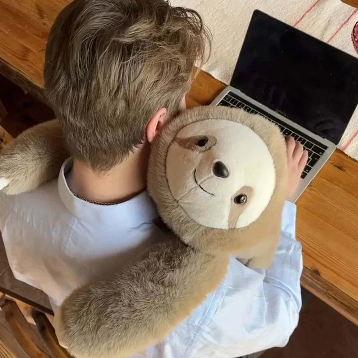Felülnézet: laptopon dolgozó férfi vállán a lajhár plüss, hosszú karjaival átöleli a nyakát és a mellkasát. 9