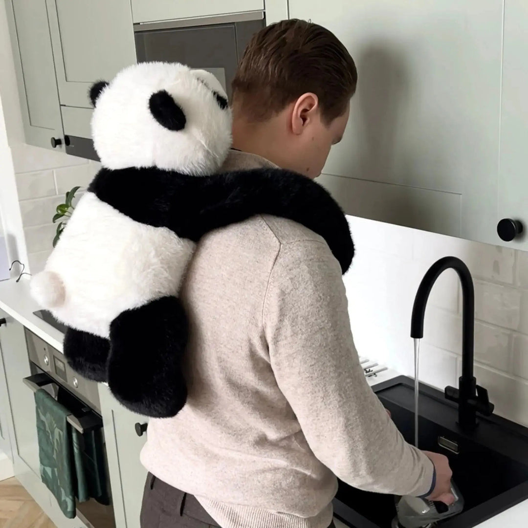 Konyhai mosogatónál álló férfi hátán a panda plüss lóg, hosszú fekete karjai a nyaka körül fonódnak. 10