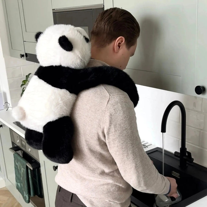 Konyhai mosogatónál álló férfi hátán a panda plüss lóg, hosszú fekete karjai a nyaka körül fonódnak. 10