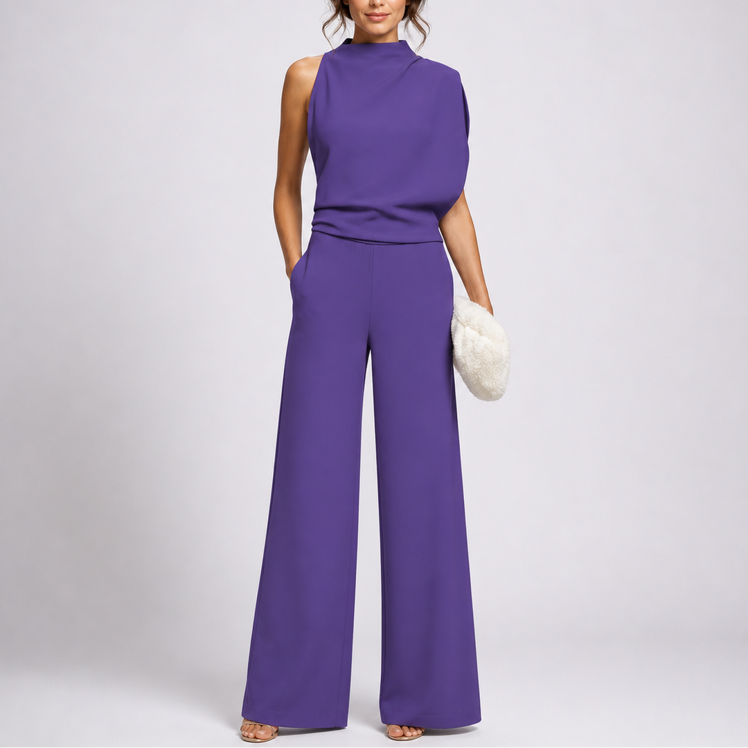 Lila, aszimmetrikusan omló felsőrészű jumpsuit modellen, bő szárral, sarokpántos szandállal és fehér táskával 3