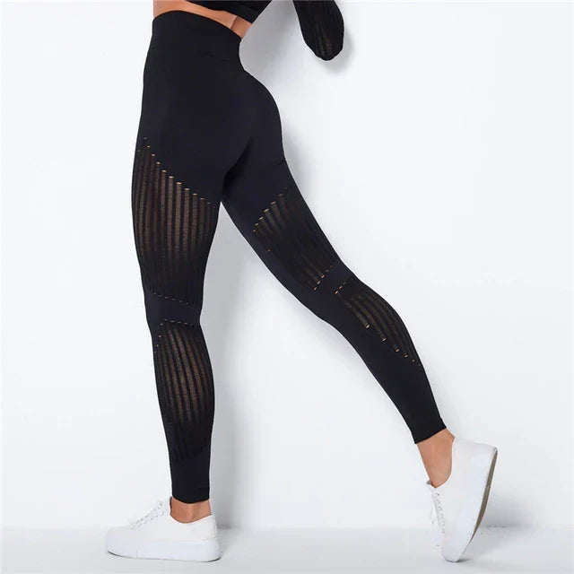 Fekete leggings hátulról, combon és vádlin áttört csíkos betétekkel, fehér sportcipővel viselve 2