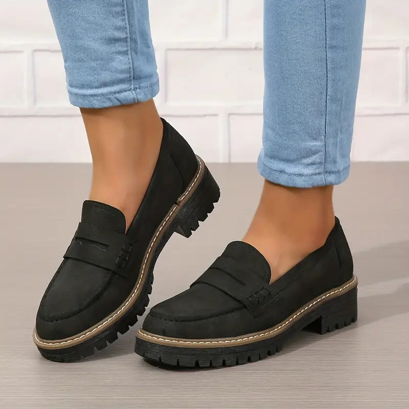 Fekete loafer vastag bordázott talppal, világoskék farmerrel viselve, az egyik láb kissé megemelve. 6