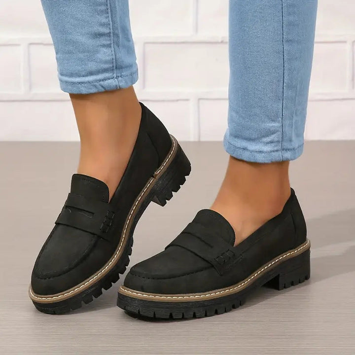 Fekete loafer vastag bordázott talppal, világoskék farmerrel viselve, az egyik láb kissé megemelve. 6