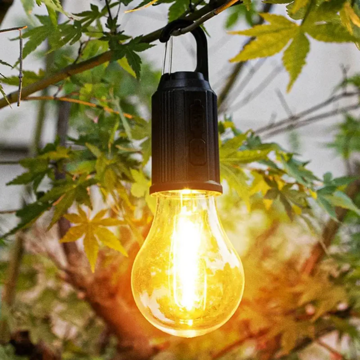 Fekete foglalatú, világító izzós lámpa faágra akasztva, juharlevelek között a szabadban 8